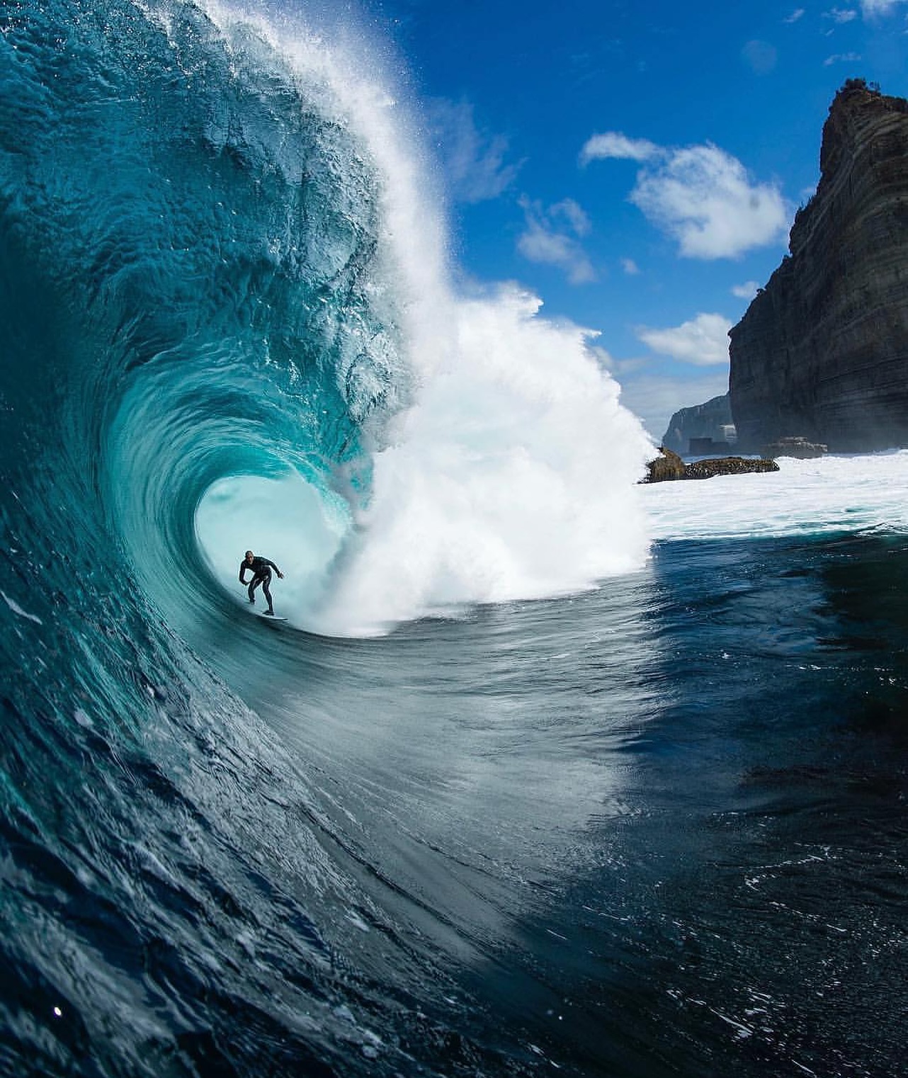 A surfer riding a large wave at Shipstern Bluff beneath Tasman Peninsula cliffs